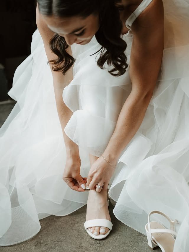 A Mockingbird Bridal bride fastening her shoe in a layered tulle gown